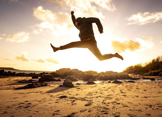 Sunset with a man jumping in a star shap on a deserted sandy beach.